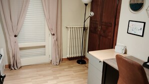 A room with a wooden floor, a radiator, a desk with a chair, a lamp, and a door. - A warm and cozy home just 5 minutes from the city of Carcassonne. Quiet surroundings (CAZILHAC)