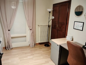 A room with a wooden floor, a radiator, a desk with a chair, a lamp, and a door. - A warm and cozy home just 5 minutes from the city of Carcassonne. Quiet surroundings (CAZILHAC)