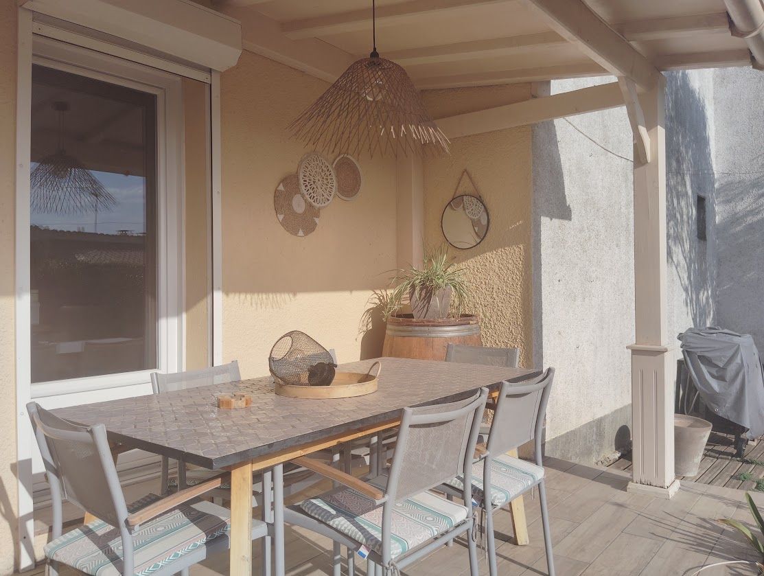 Een terras buiten met een tafel, stoelen, een hanglamp en een bloempot.