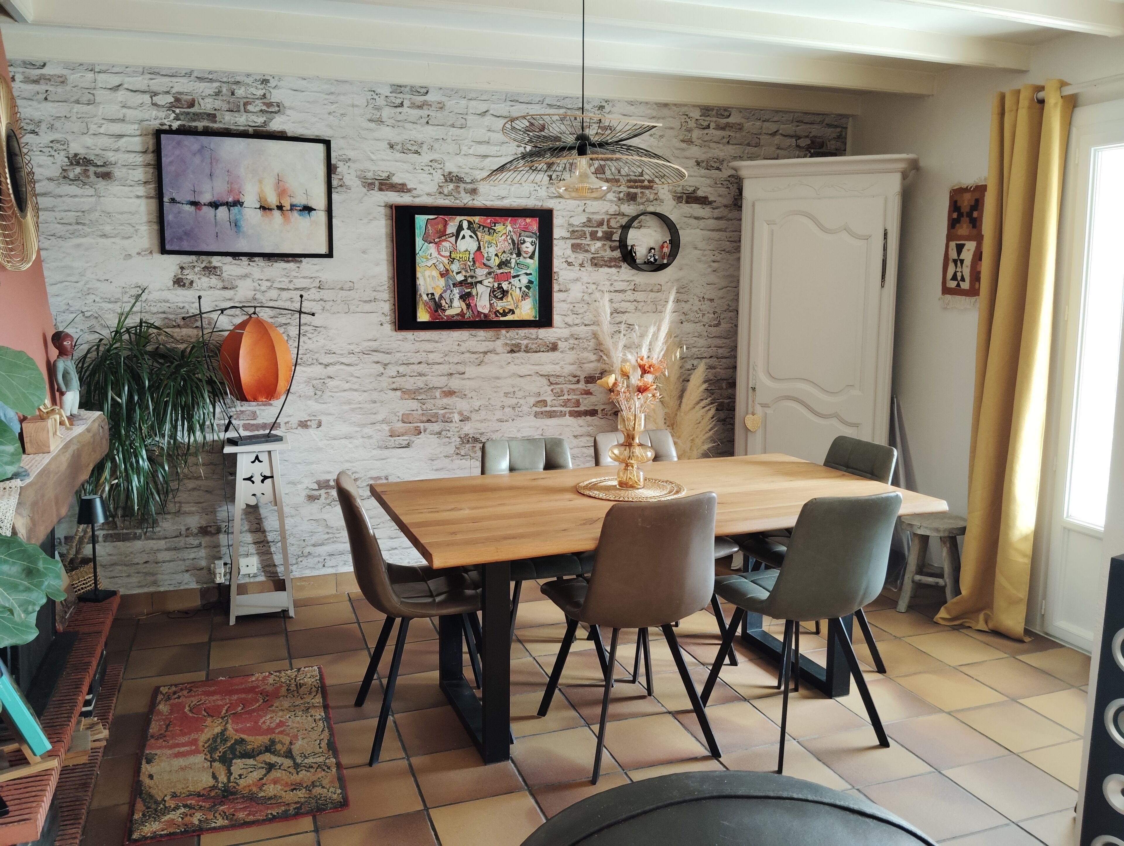 A dining area with a wooden table, chairs, and a brick wall with artwork.