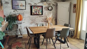 A dining area with a wooden table, chairs, and a brick wall with artwork. - A warm and cozy home just 5 minutes from the city of Carcassonne. Quiet surroundings (CAZILHAC)