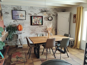 A dining area with a wooden table, chairs, and a brick wall with artwork. - A warm and cozy home just 5 minutes from the city of Carcassonne. Quiet surroundings (CAZILHAC)