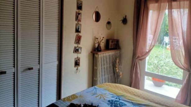 A bedroom with a bed, a radiator, a window with curtains, and a wall with pictures. - A warm and cozy home just 5 minutes from the city of Carcassonne. Quiet surroundings (CAZILHAC)