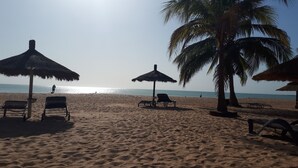 Une plage avec des parasols en chaume et des chaises longues.