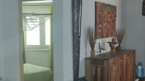 Une pièce avec un plafond haut, un escalier en bois, un lit recouvert d’une couverture verte, une armoire en bois ornée d’objets décoratifs et un grand tableau accroché au mur.