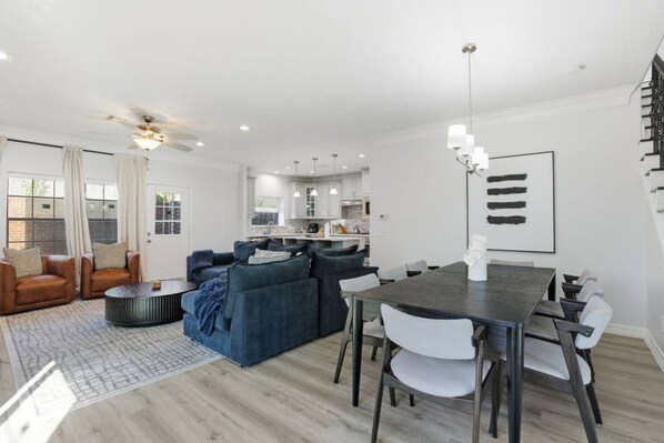A modern living room with a dark wood dining table and white chairs, a blue sofa, and a ceiling fan. - SW Houston 3BR Sleeps 10 | 2 Living Areas (Houston)