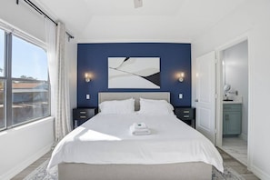 A hotel room with a large bed, two bedside tables, a nightstand, a bathroom with a sink and mirror, and a view through a window. - SW Houston 3BR Sleeps 10 | 2 Living Areas (Houston)