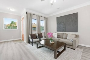 Un salon spacieux comprenant un canapé, deux fauteuils, une table basse et une grande fenêtre avec des rideaux.