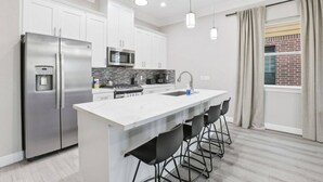 A modern kitchen with a stainless steel refrigerator, a microwave, and a water dispenser. There is a large island with bar stools and a sink. - SW Houston 2BR | King Beds, Pets Welcome (Houston)