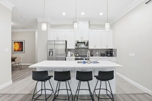 Une cuisine moderne dotée d’un îlot central, de tabourets de bar, d’appareils électroménagers en acier inoxydable et de luminaires suspendus.
