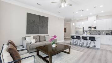 A modern living room with a sofa, coffee table, and a dining area with bar stools.