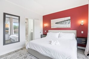 Un dormitorio con una cama grande, un espejo, un cuadro y una pared de acento roja.