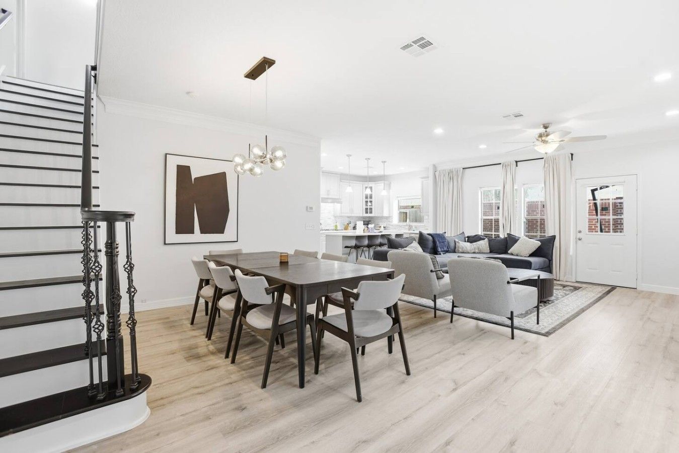 A modern interior with a dining area, sofa set, staircase, and kitchen.
