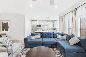 A modern living room with a sectional sofa, a coffee table, and a view of a kitchen and dining area.