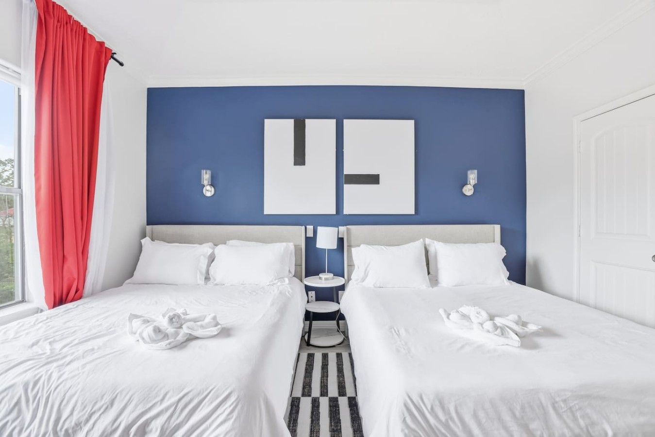 A double bed with white bedding, a blue accent wall, and a red curtain.