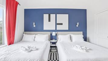 A double bed with white bedding, a blue accent wall, and a red curtain.