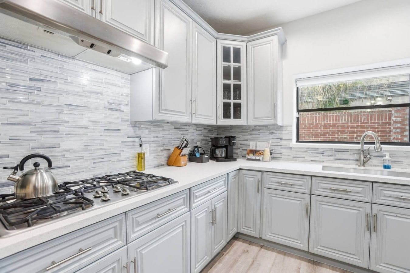 A modern kitchen with white cabinetry, a gas stove, and a window with a view of a brick wall.