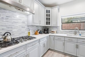 Una cocina moderna con muebles blancos, una estufa a gas y un ventanal con vista a un muro de ladrillo.
