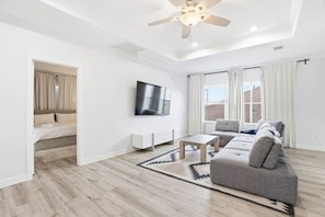 A modern living room with a grey sofa, a coffee table, and a flat-screen TV mounted on the wall.
