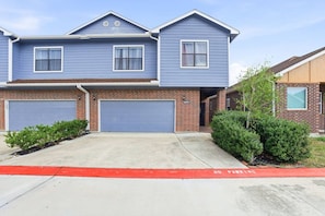 A two-story residential building with a blue exterior, two garage doors, and a red curb indicating no parking.
