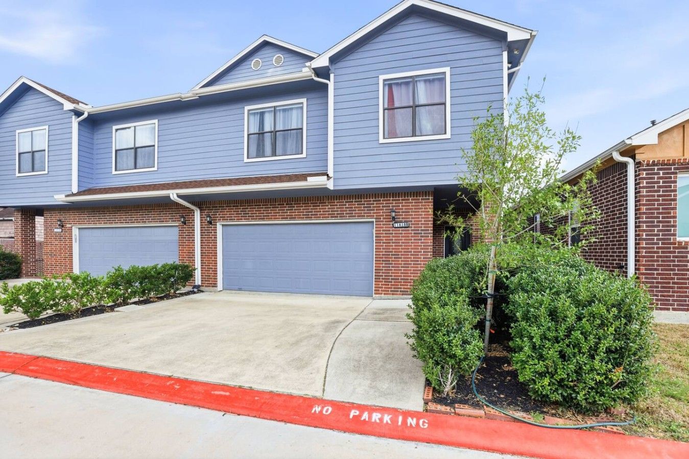 A two-story residential building with a blue exterior, two garage doors, and a red 'No Parking' sign in the foreground.