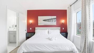 A bedroom with a bed, two bedside tables, a nightstand, a window with curtains, and a painting on the wall.