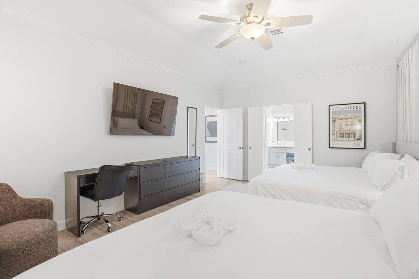 A hotel room with a bed, a desk, a chair, a ceiling fan, and a door leading to a bathroom.