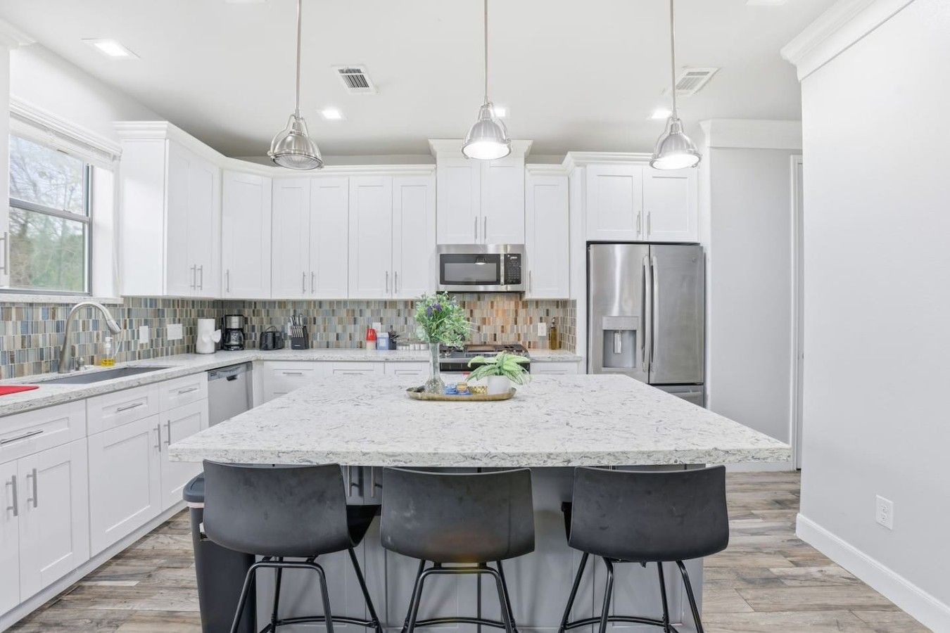 A modern kitchen with white cabinets, a large island with bar stools, stainless steel appliances, and pendant lighting.