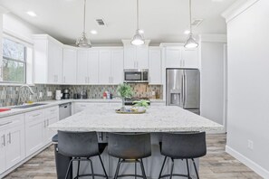 A modern kitchen with white cabinets, a large island with bar stools, stainless steel appliances, and pendant lighting. - SW Houston 1BR | King Bed, Sleeps 4 (Houston)