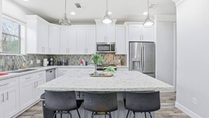 Una cocina moderna con armarios blancos, una isla grande con taburetes de bar, electrodomésticos de acero inoxidable e iluminación colgante.