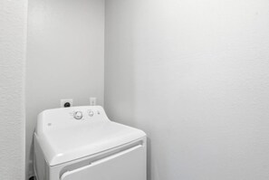 Lavadora blanca en una esquina, con un enchufe de pared.