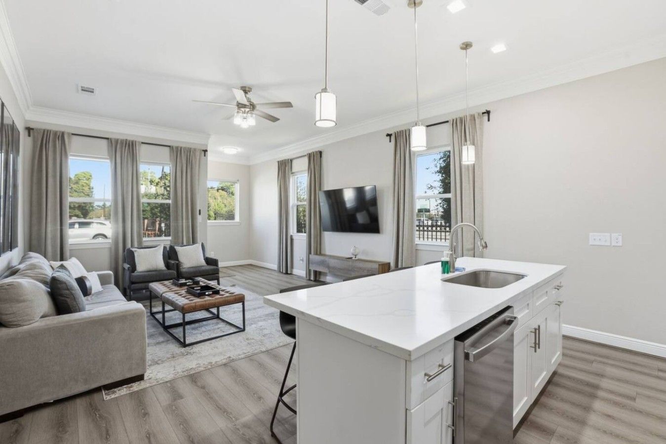 A modern living room with a sofa, coffee table, and TV. There's a kitchen with a large island and a dining area.