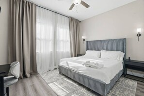 Habitación de hotel con cama, escritorio, silla, ventilador de techo y ventana con cortinas.