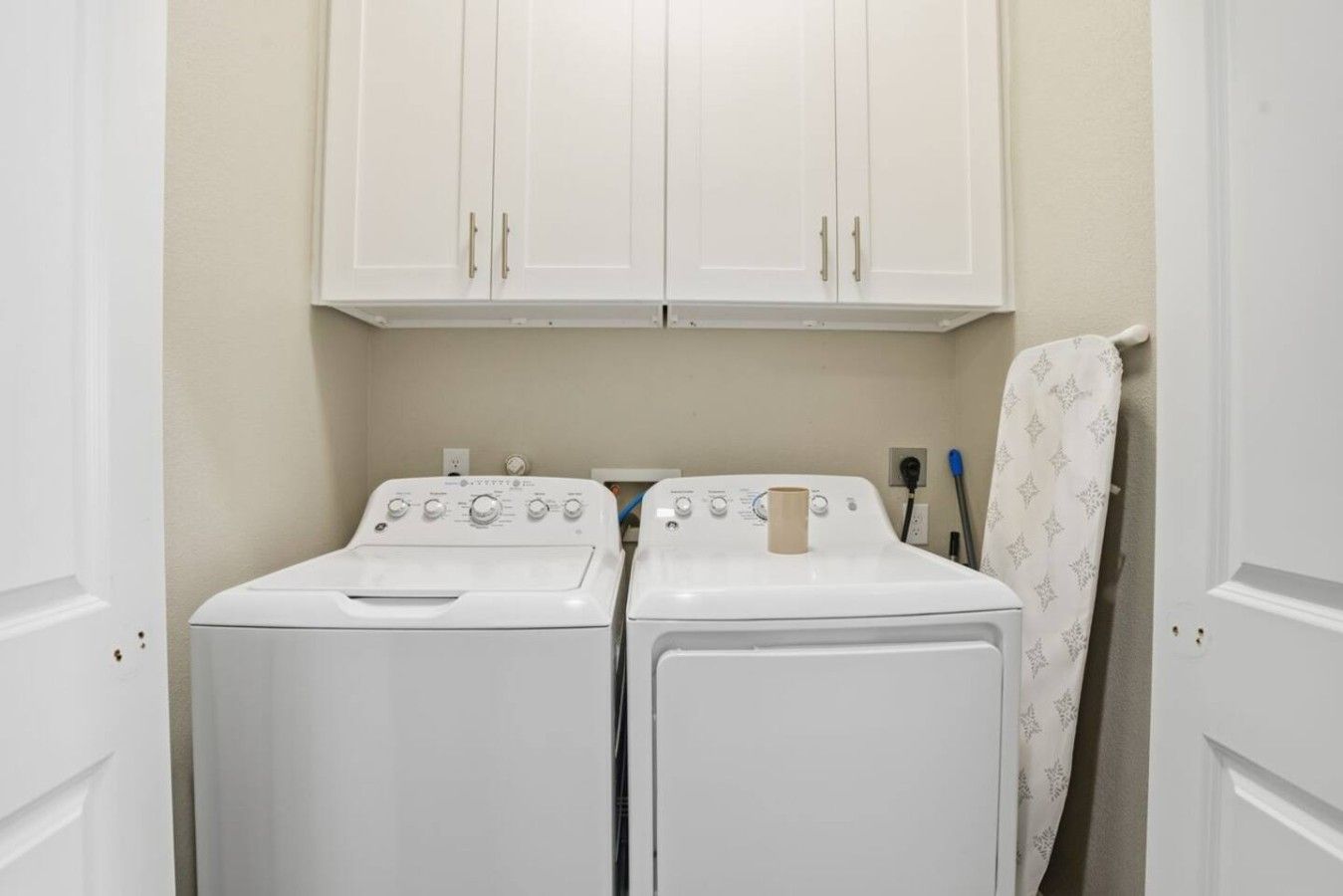 A laundry room with two white front-loading washing machines, a white cabinet above, and a towel hanging on the wall.