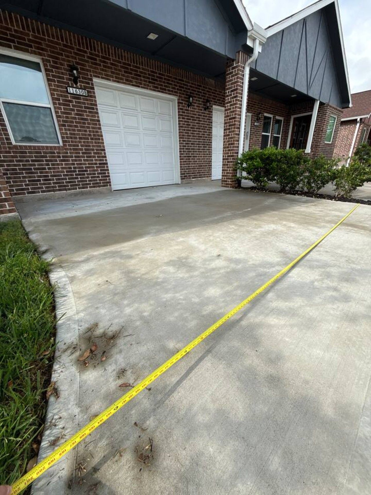 Une allée menant à une maison, avec un mètre ruban, une porte de garage et une maison en briques.