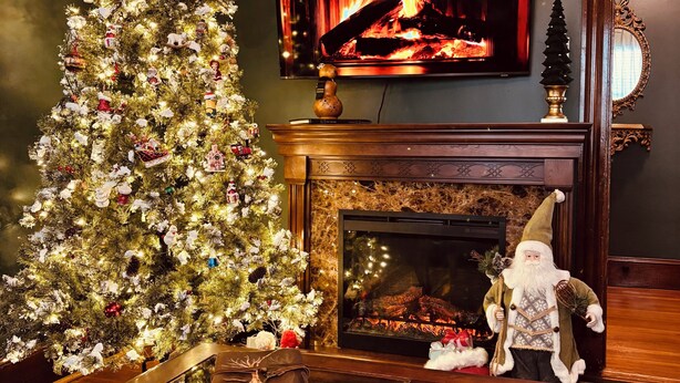 Una sala de estar acogedora con un árbol de Navidad, una chimenea, un televisor y una figura decorativa de Papá Noel.