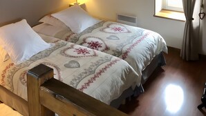 A bedroom with a wooden bed frame, two white pillows, a bedside table with a lamp, a window with curtains, and a wall-mounted artwork.