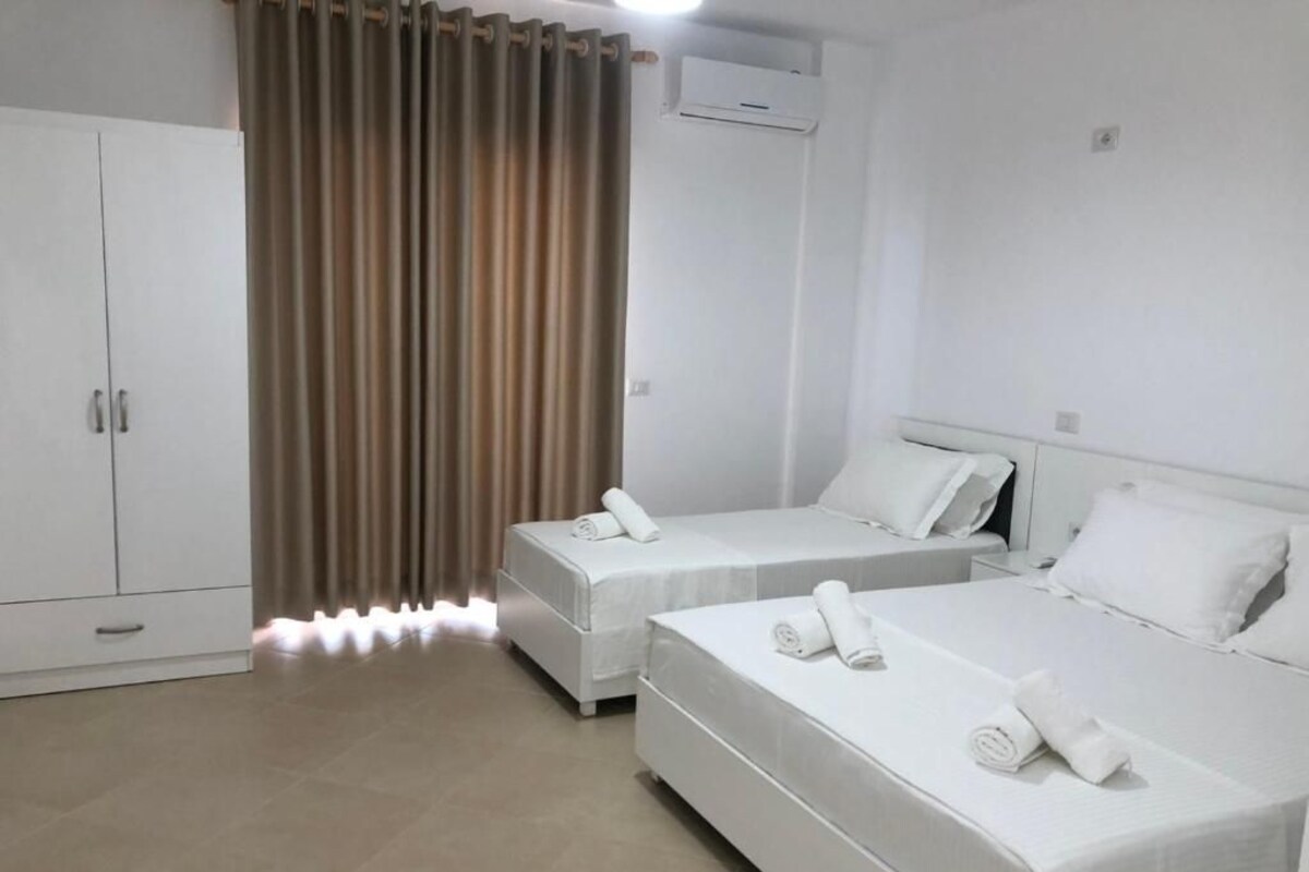A hotel room with two single beds, a wardrobe, and a curtain.