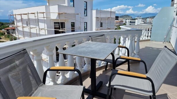 Une terrasse sur le toit, avec une table et des chaises, des balustrades blanches et une vue sur un immeuble blanc en construction.