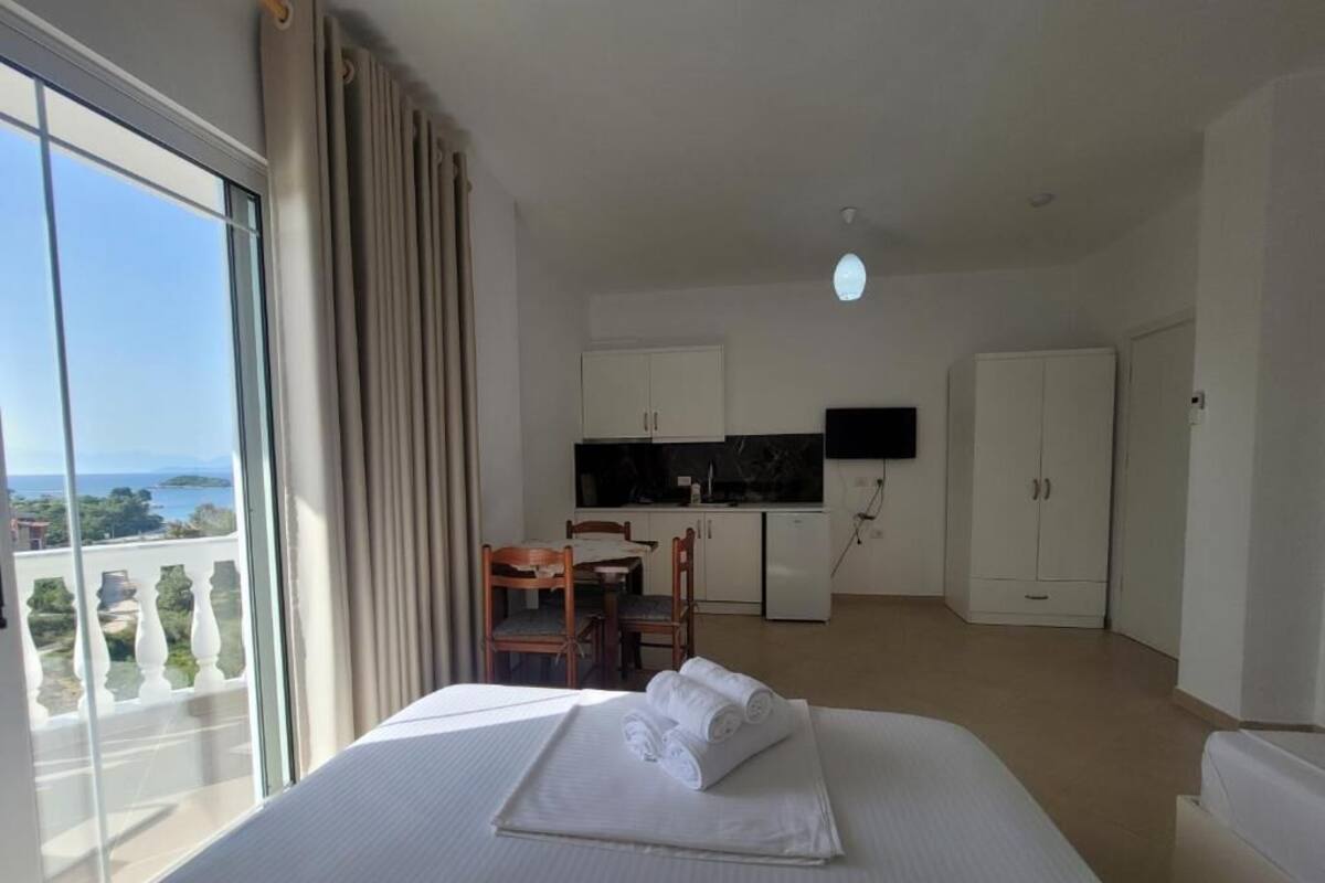 A hotel room with a bed, a desk, a chair, a television, and a view of the sea.