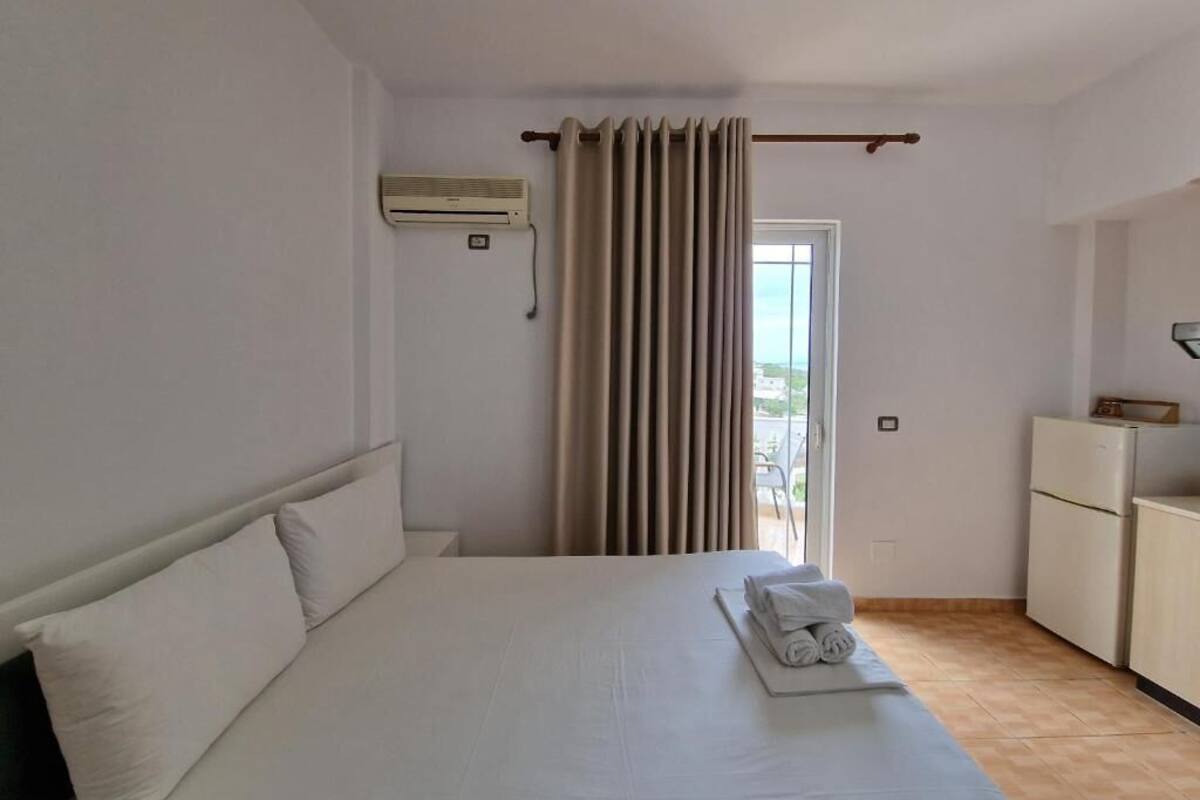 A hotel room with a bed, a small kitchenette, and a window with curtains.
