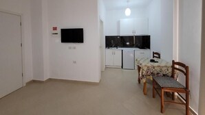 Un espace de vie compact comprenant un coin repas, une kitchenette et un téléviseur fixé au mur.