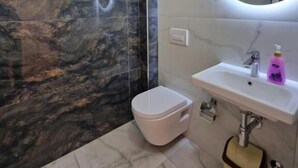 Une salle de bain avec un mur en marbre, des toilettes, un lavabo avec un miroir et un distributeur de savon.