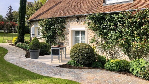 Une maison en pierre avec un toit en tuiles, un chemin pavé et un petit jardin.