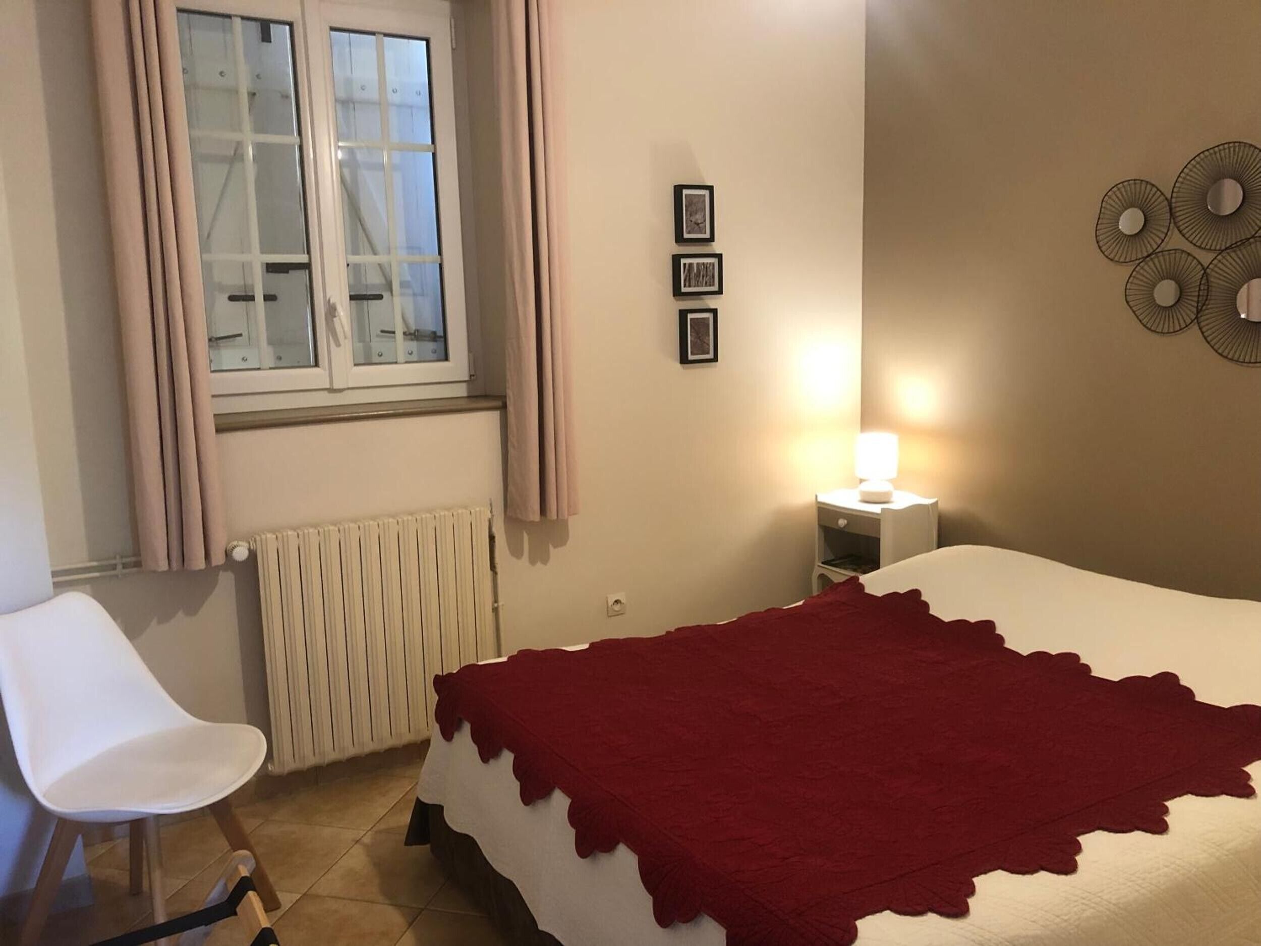 A bedroom with a bed, a chair, a window, a radiator, and wall decorations.