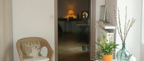 A room with a wicker chair, a small table with a plant, and a doorway leading to another room.