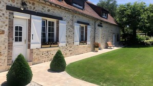 Un bâtiment en pierre avec des volets blancs, une entrée pavée et une pelouse bien entretenue.