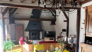 Un coin repas avec une table en bois, des chaises jaunes, un lustre et une cuisine en arrière-plan.