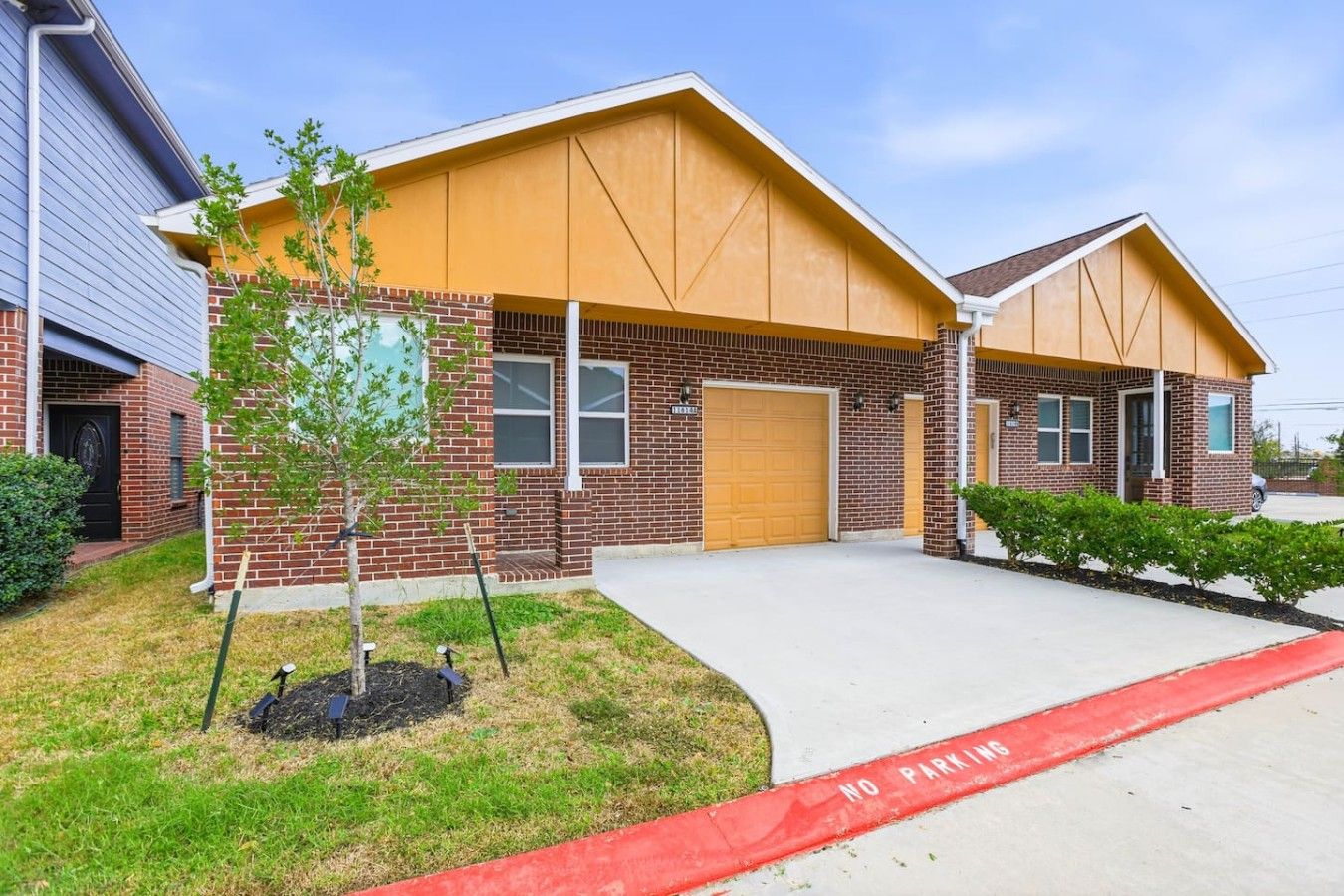 A two-story building with a brick facade, a garage, and a small tree in the front yard.