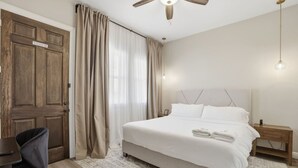 Une chambre à coucher comprenant un lit, une table de chevet, un bureau, une chaise, un ventilateur de plafond et une porte.